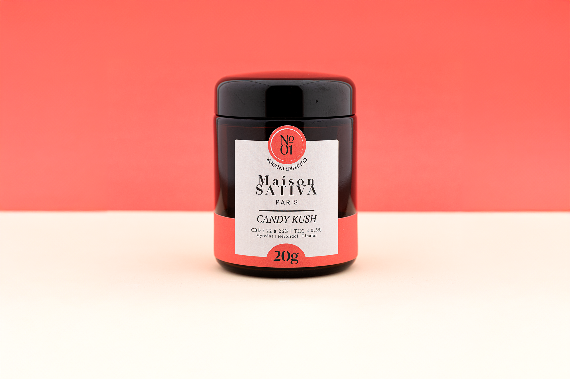 pot en verre ambré de 20 grammes de Candy Kush sur fond rouge.