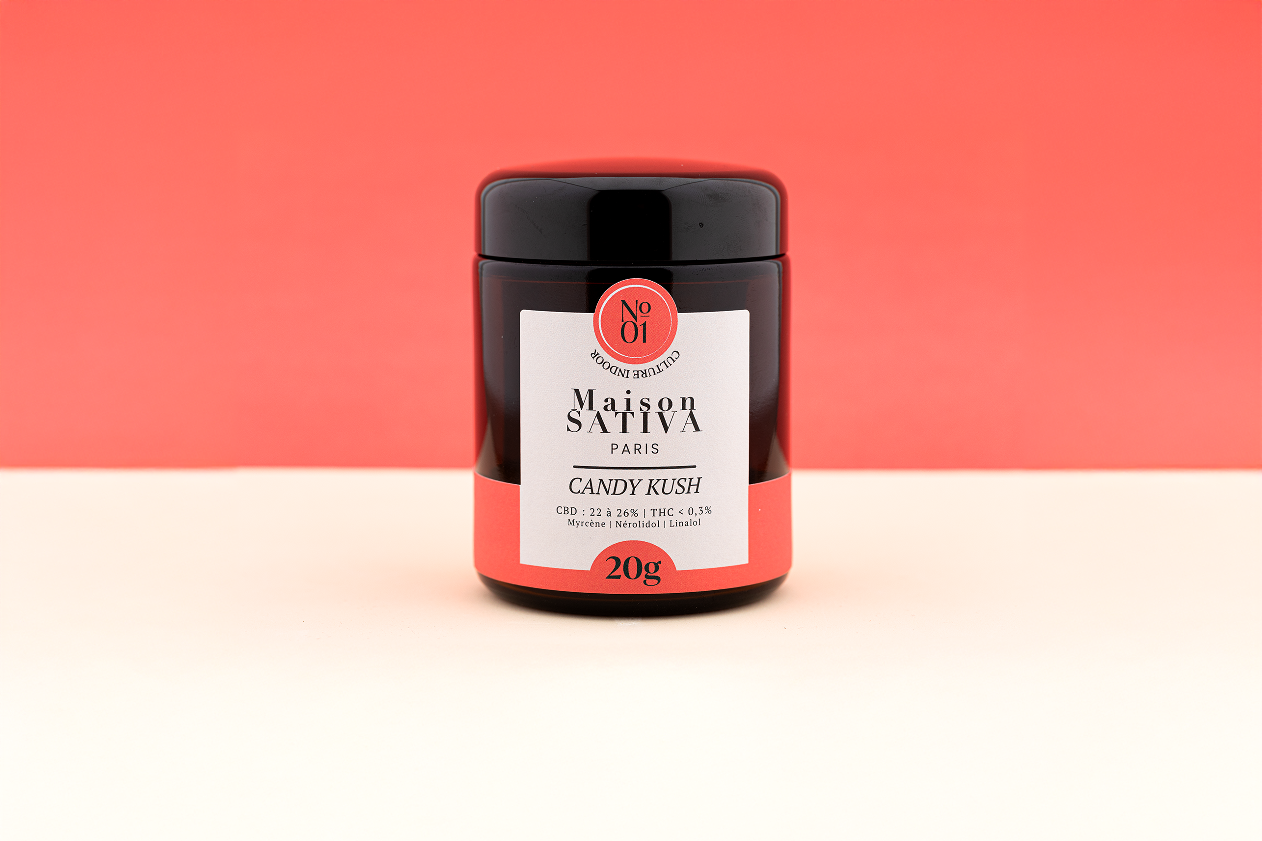 pot en verre ambré de 20 grammes de Candy Kush sur fond rouge.