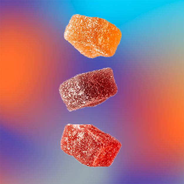 Trois gummies THC colorés en suspension sur fond dégradé