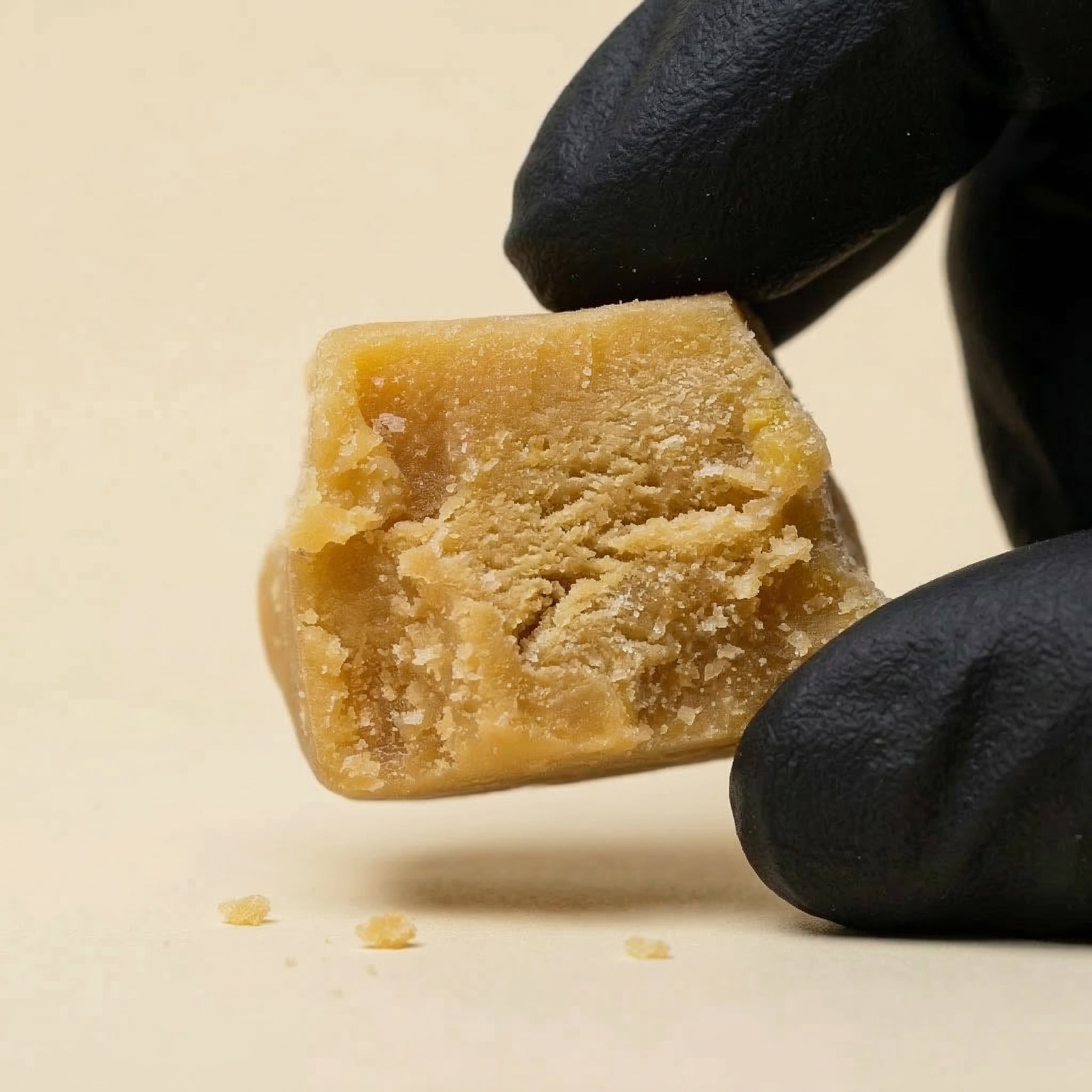 Morceau malléable de résine CBD Ice O Lator Mango tenu par des gants noirs, illustrant la qualité premium et la pureté du produit.