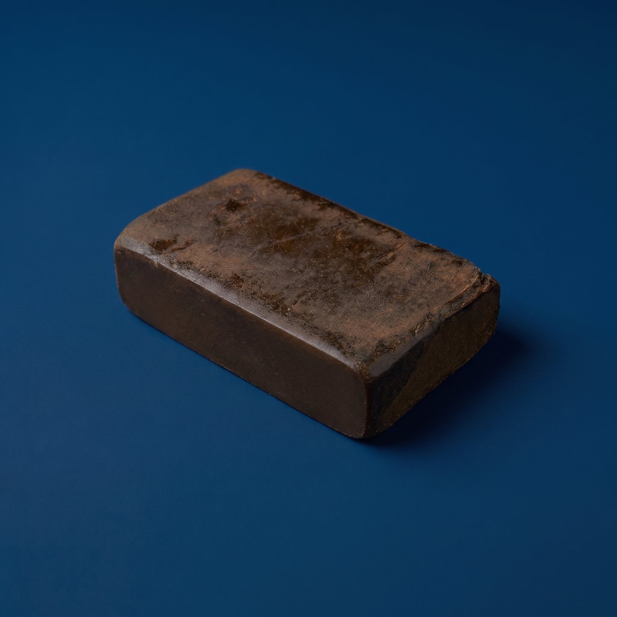 Bloc entier et compact de résine de canabise légale 3x filtré Maison Sativa sur fond bleu, illustrant la densité d'un hash issu d'un triple tamisage.