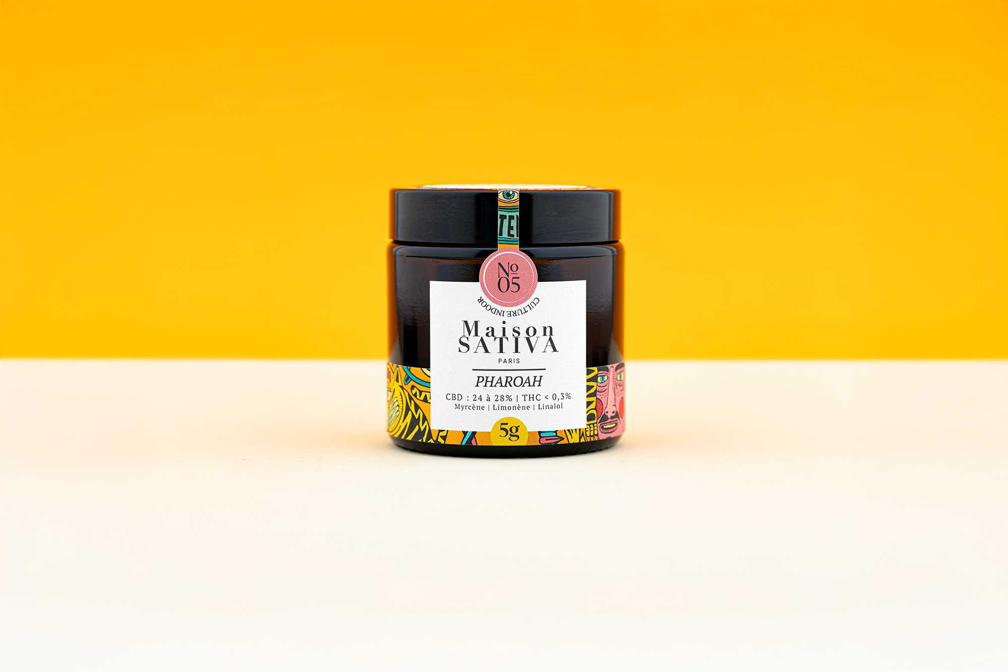 Pot en verre ambré de fleurs de CBD Pharoah de la marque maison sativa sur fond jaune. 