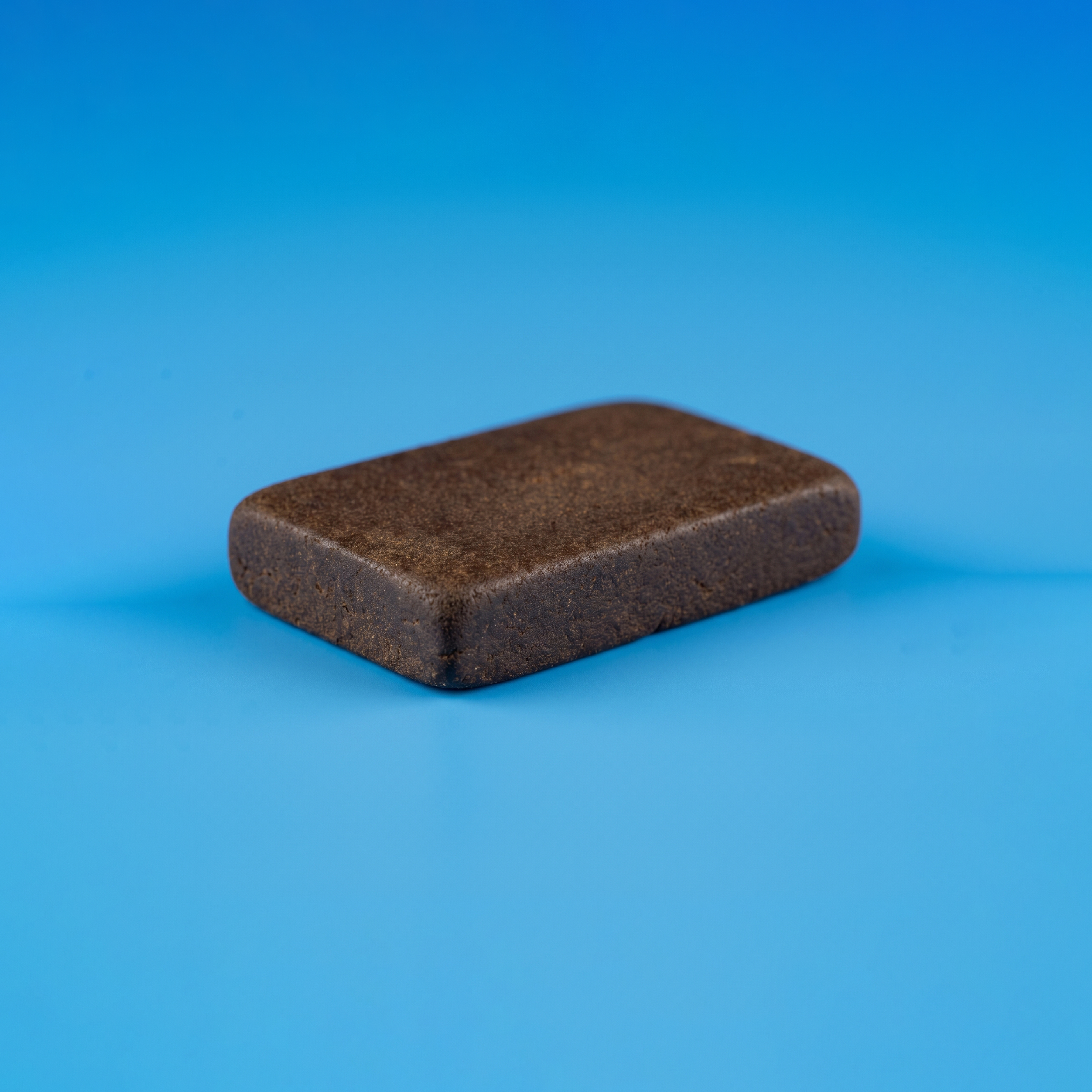 Bloc entier et compact de résine de canabise légale 3x filtré Maison Sativa sur fond bleu, illustrant la densité d'un hash issu d'un triple tamisage.