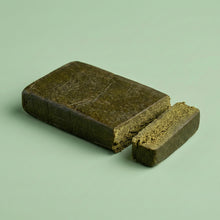 Bloc rectangulaire de résine CBD 3x filtré sur fond vert, avec une tranche coupée révélant une texture interne granuleuse et riche.