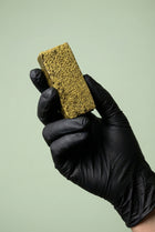 Main gantée de noir présentant une barre verticale de résine de cannabis légal à la texture dense et jaune-verte.