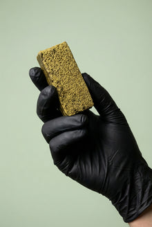 Main gantée de noir présentant une barre verticale de résine de cannabis légal à la texture dense et jaune-verte.