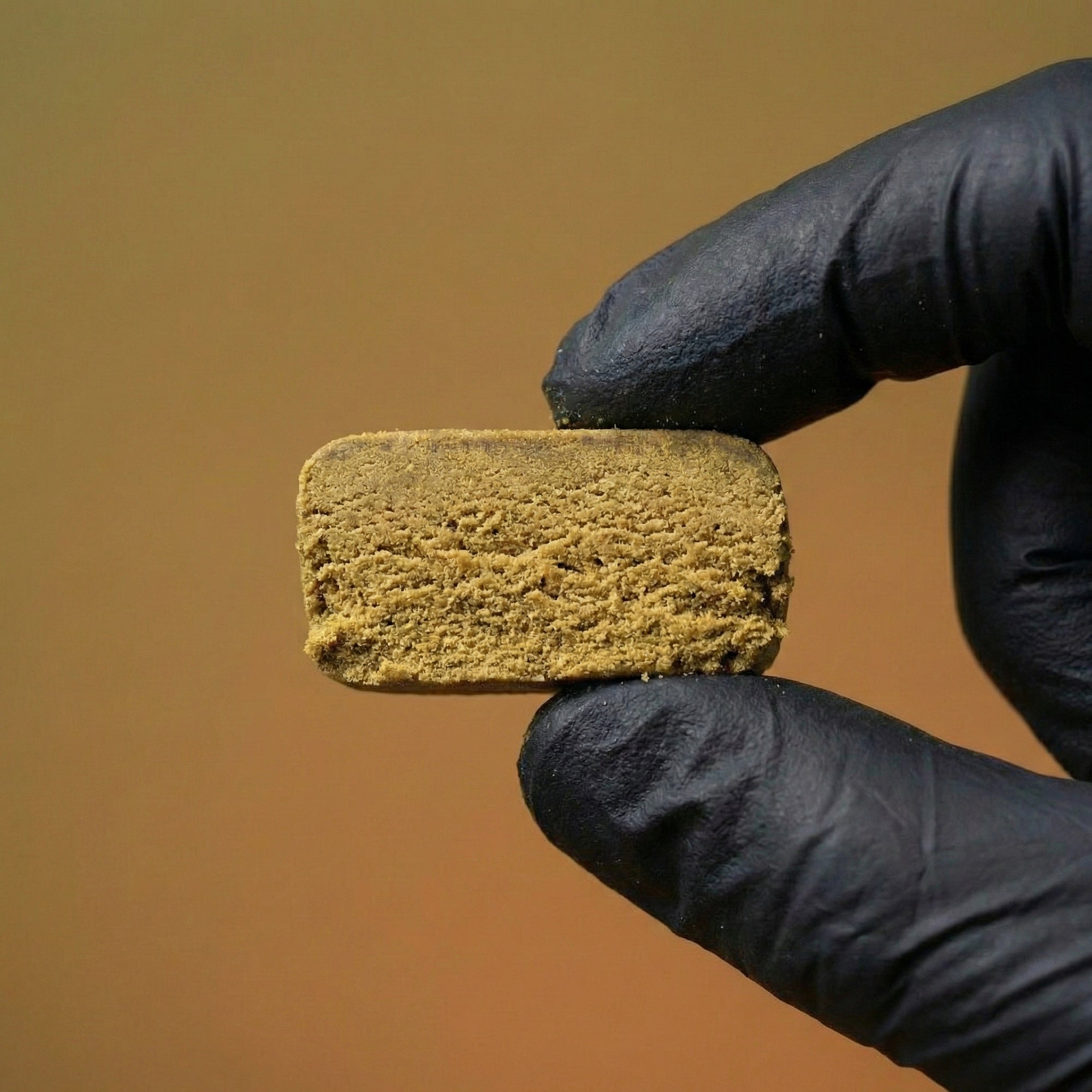 Tranche de résine de cbd puissante IMPERIAL JAUNE 60% HRC de chez Maison Sativa. La résine est tenue par deux doigts gantés.