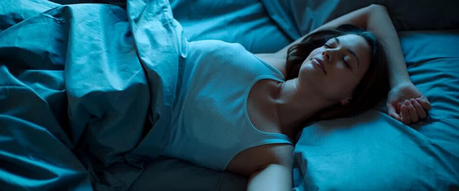 jeune femme dort paisiblement dans un lit aux couvertures bleues. 