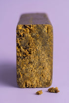 Gros plan sur l'intérieur d'un bloc de Static Hash CBD révélant une texture dorée, sableuse et facilement effritable